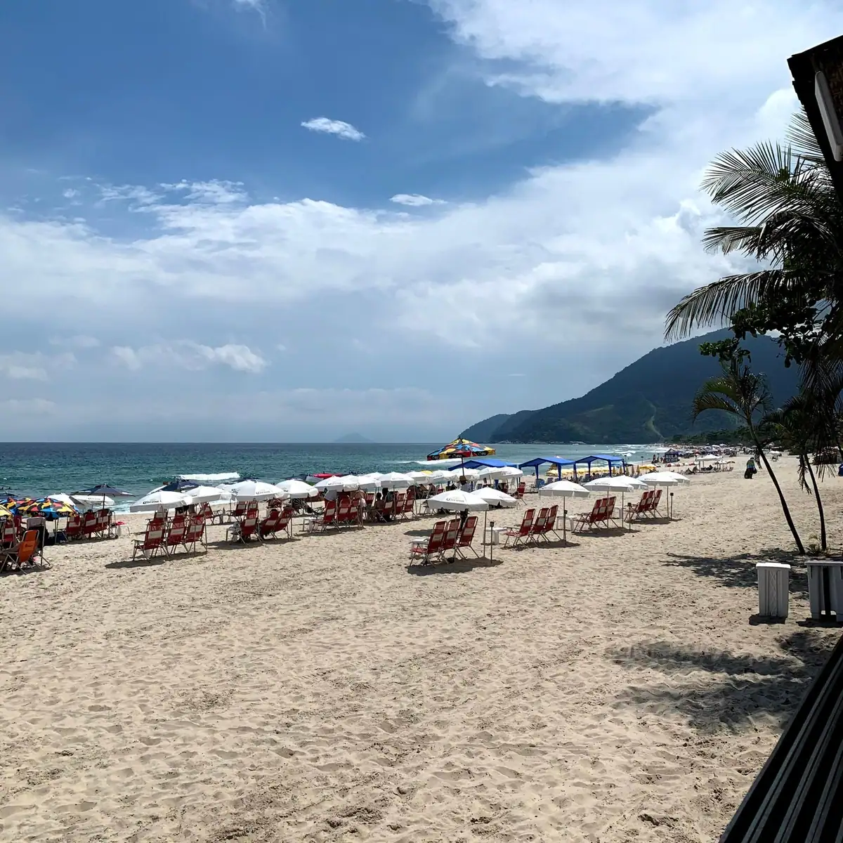 Stretch of sand on Maresias beach with beach umbrellas and a hill in the background